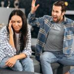 Familienpaar sitzt auf einem Sofa im Wohnzimmer, ein wütender Mann schreit wütend eine Frau an, die Frau wendet sich von ihm ab, schließt traurig und enttäuscht die Augen, Symbol für Familienstreit, Meinungsverschiedenheiten und Missverständnisse.