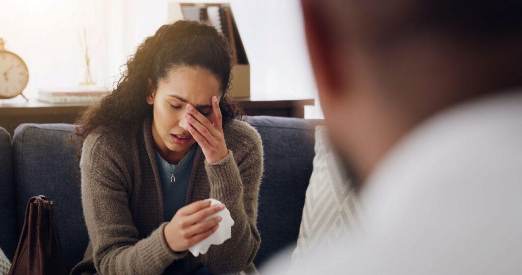 Frau sitzt traurig mit Taschentuch und wird von einem Gespraechspartner begleitet – Darstellung emotionaler Kompetenz und psychologischer Sensibilitaet in der Trauerredner Ausbildung.