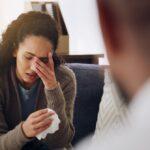 Frau sitzt traurig mit Taschentuch und wird von einem Gespraechspartner begleitet – Darstellung emotionaler Kompetenz und psychologischer Sensibilitaet in der Trauerredner Ausbildung.